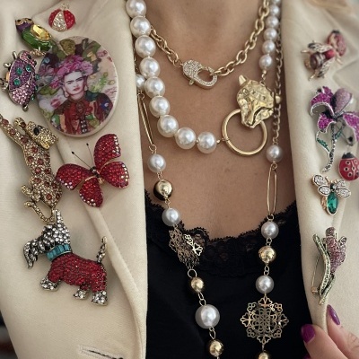 Blazer creme com broches coloridos e colares dourados e pérolas