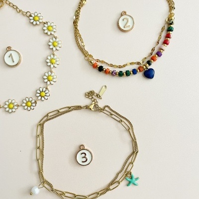 Três pulseiras coloridas e pendentes em fundo claro