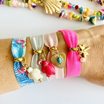 Pulseiras elásticas coloridas com pendentes e colares variados ao fundo