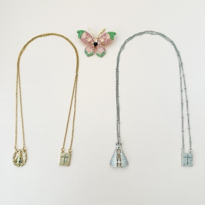 Dois colares com pendentes e um broche de borboleta colorido sobre fundo branco