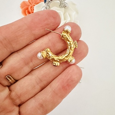 Brinco dourado com pérolas em fundo branco e mão segurando.