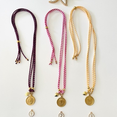 Três colares trançados coloridos com pendentes dourados numerados, e broche de flor branco e amarelo