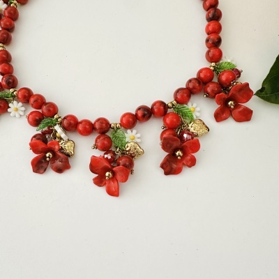 Colar com contas vermelhas, flores vermelhas e brancas, folhas verdes e detalhes dourados.