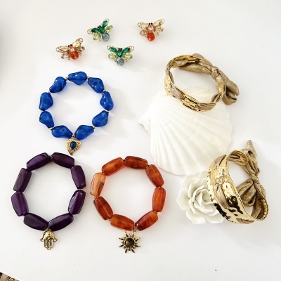 Conjunto de bijuterias coloridas com pulseiras e brincos dispostos sobre superfície branca