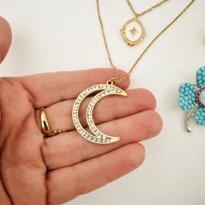 Colar dourado com pendente lua crescente com pedras brilhantes na mão de pessoa.