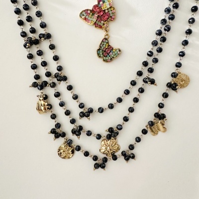 Colar com contas pretas e pingentes dourados em formas de flores e borboletas, com detalhe de borboletas coloridas com pedras.