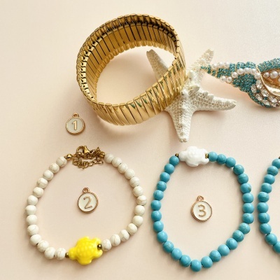 Pulseiras elásticas e colares com contas em cor dourada, branca e azul em fundo bege