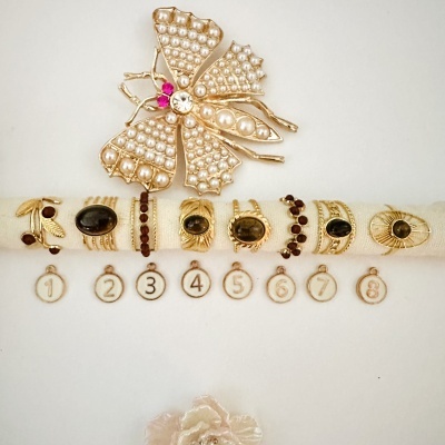 Anéis dourados numerados sobre tecido creme e broche de borboleta dourado com pérolas
