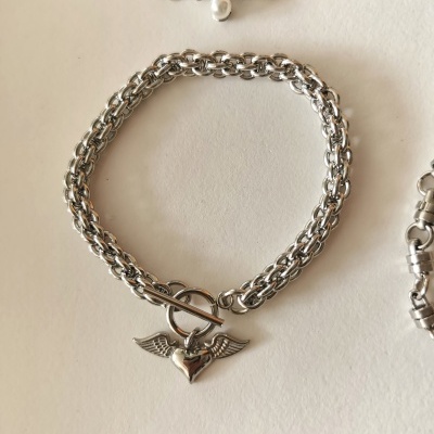 Pulseira prateada com coração alado e fecho toggle.