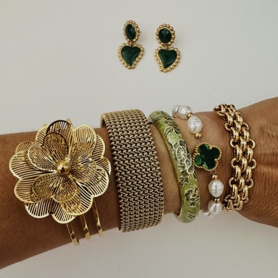 Conjunto de brincos dourados com pedras verdes e pulseiras em diferentes estilos num braço