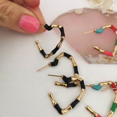 Brincos argola dourados e pretos imitando bambu com mãos segurando um, em superfície branca com decoração