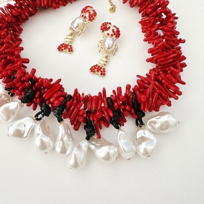 Colar vermelho com pedras e pérolas penduradas e brincos dourados com detalhes vermelhos e pérola.