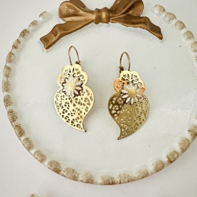 Brincos dourados com flores brancas sobre prato decorativo branco e laço castanho