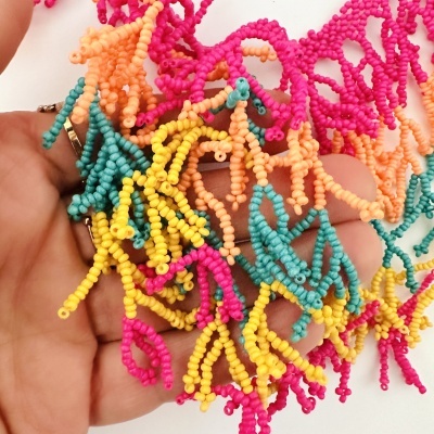 Colar ou pulseira colorida de missangas em tons de rosa, azul, amarelo e laranja sendo segurada por uma mão.