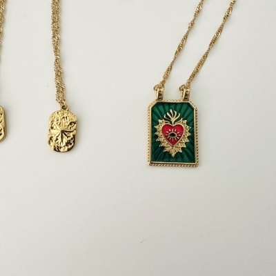 Colares com pendentes dourados, um com fundo verde e coração e outro com relevo floral