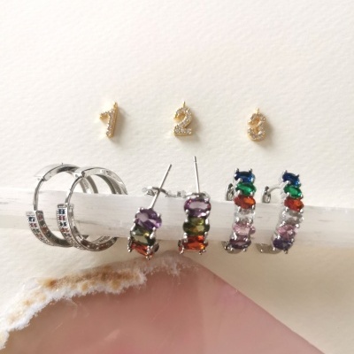 Seis brincos em três pares com pedras coloridas e numeração 1, 2, 3 em pequenos pendurais dourados