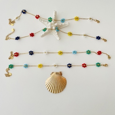 Pulseiras ou colares dourados com flores coloridas e detalhes de pérolas sobre fundo branco com estrela-do-mar e concha