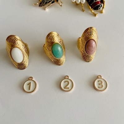 Três anéis dourados com pedras coloridas, dois broches de abelha e três medalhas numeradas