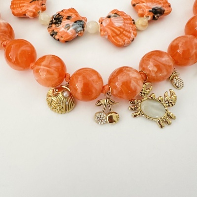 Colar com contas laranja e pendentes dourados em forma de conchas, cerejas e caranguejo