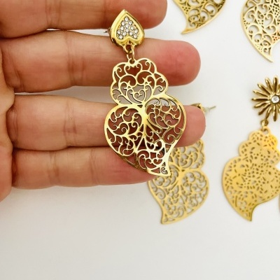 Brinco dourado com corações filigranados e cristais segurado por mão