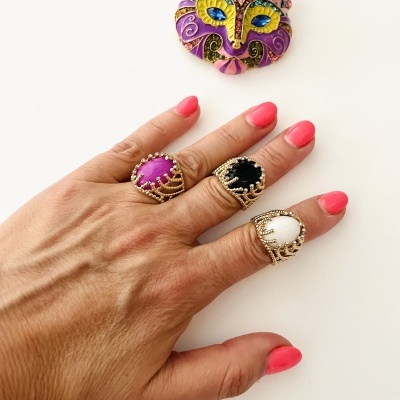 Mão com três anéis dourados com pedras coloridas e broche de raposa colorida sobre fundo branco