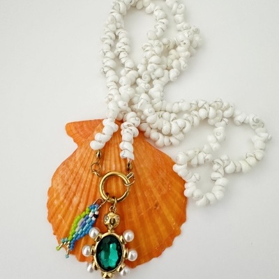 Colar branco com pendente dourado e verde sobre concha laranja