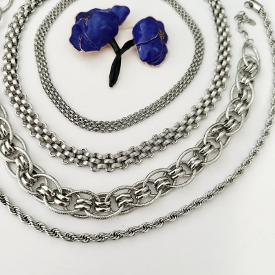 Colares de metal prateado e broche de flores azuis sobre fundo branco