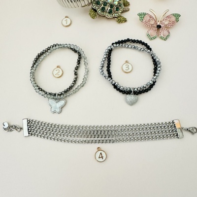 Quatro acessórios, incluindo pulseiras de contas e bracelete de malha metálica prateada, sobre fundo claro.