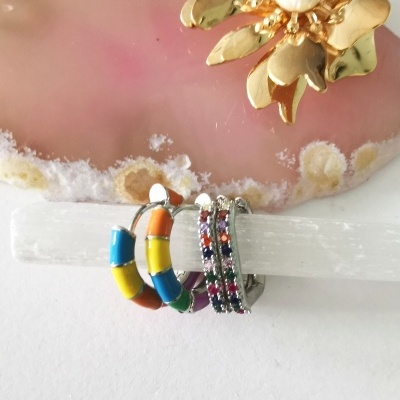 Brincos coloridos e prateados com pedras, com broche dourado e pedra rosa ao fundo
