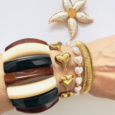 Braço com pulseiras de vários estilos em fundo branco com flor decorativa