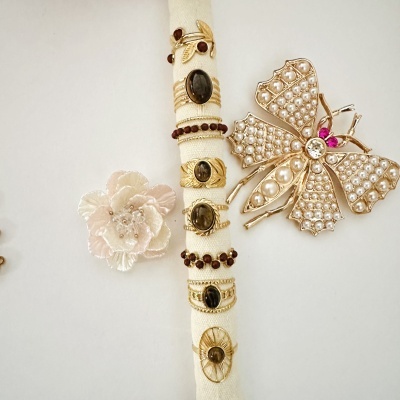 Anéis dourados com pedras castanhas e broches decorativos sobre fundo branco