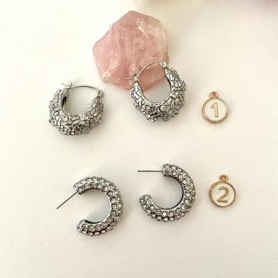 Brincos prateados texturizados com pendentes numerados sobre superfície branca