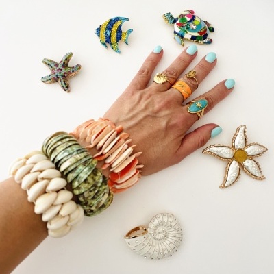 Pulseiras e anéis de conchas e broches coloridos em forma de animais marinhos sobre fundo branco