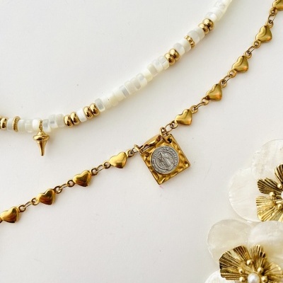 Dois colares, um com contas brancas e douradas e outro dourado com corações, sobre fundo branco com flores decorativas