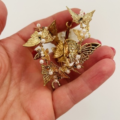 Brincos dourados com borboletas e pérolas na mão