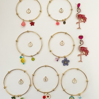 Sete pulseiras douradas com pendentes coloridos e dois brincos de flamingo com pedras cor de rosa