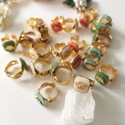 Anéis dourados com faces quadradas coloridas e símbolo dourado sobre superfície branca