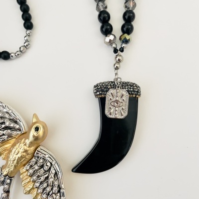 Colar com dente preto e detalhes prateados ao lado de broche de pássaro prateado e dourado