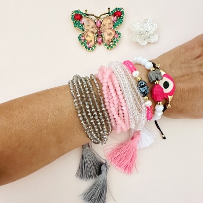 Braço com várias pulseiras coloridas e broche de borboleta colorido sobre fundo claro