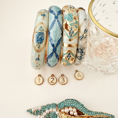 Pulseiras esmaltadas azuis e verdes com detalhes dourados, pendentes numerados e broche decorado com pérolas e pedras azuis