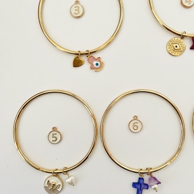 Quatro pulseiras douradas com pendentes variados e etiquetas numeradas de 3 a 6