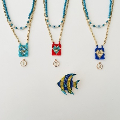 Três colares dourados com pingentes de miçangas coloridas numerados e broche de peixe colorido