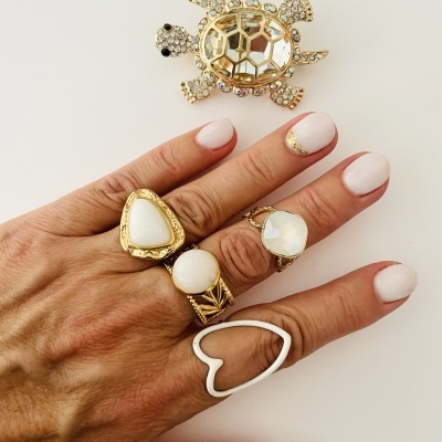 Mão com anéis dourados e brancos e broche de tartaruga dourada com pedras