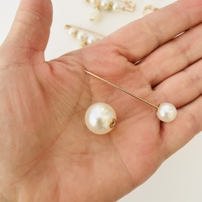 Brincos de pérola com suporte dourado em mão com fundo branco