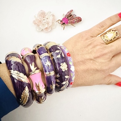 Pulseiras largas coloridas com detalhes dourados e anel numa mão sobre fundo branco