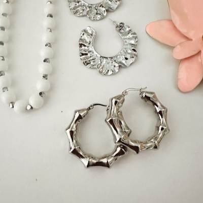 Dois pares de brincos prateados texturizados, pulseira branca com detalhes prateados e flor rosa