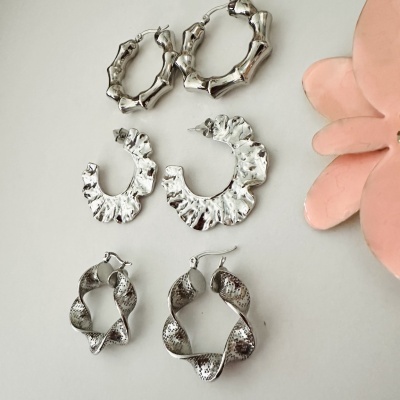 Três pares de brincos prateados com texturas variadas e flor rosa decorativa