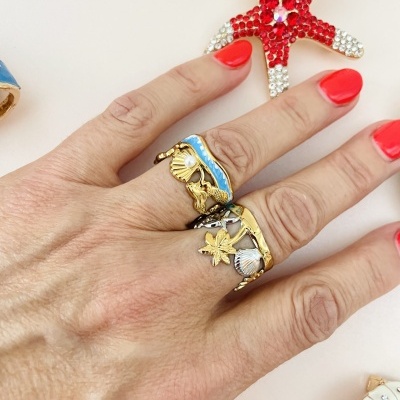 Anel dourado com conchas e estrela do mar, unha vermelha, fundo branco com estrela do mar vermelha de cristais