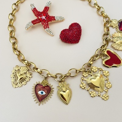 Colar dourado com vários pendentes e dois broches vermelhos com strass