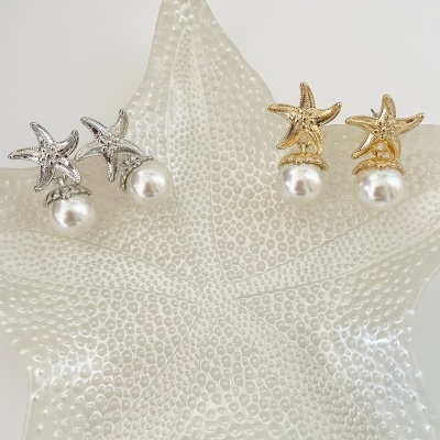 Brincos com estrela do mar e pérolas em dourado e prateado sobre peça decorativa de estrela do mar